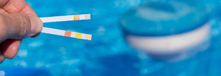 Hand hält Teststreifen im Poolwasser